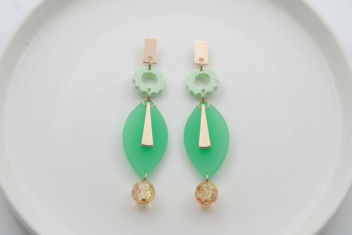 Green Nia long geometric statement earrings arranged on a white plate