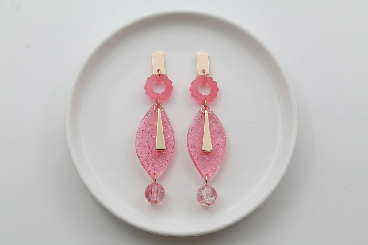 Pink Nia long geometric statement earrings arranged on a white plate