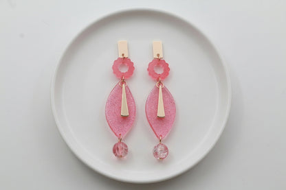 Pink Nia long geometric statement earrings arranged on a white plate