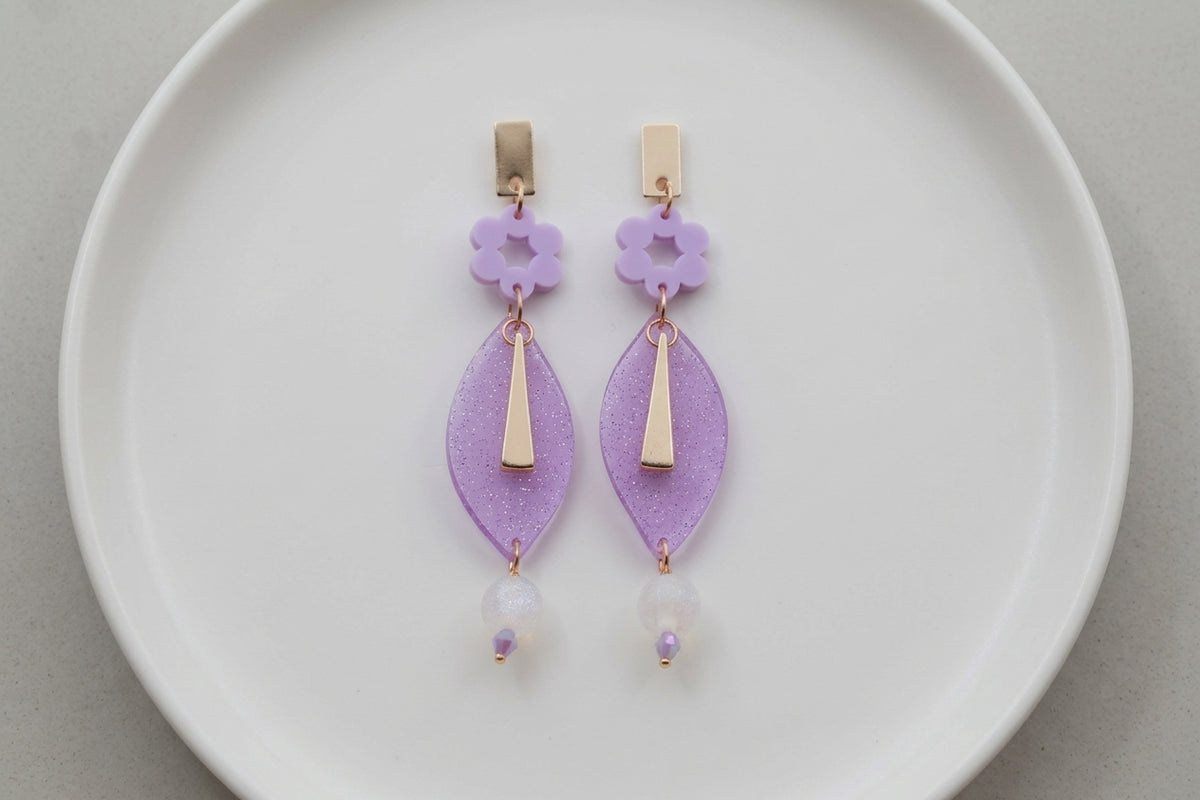 Purple Nia long geometric statement earrings arranged on a white plate