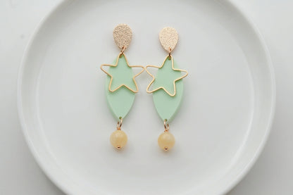 Green Nina star geometric dangle earrings arranged on a white plate