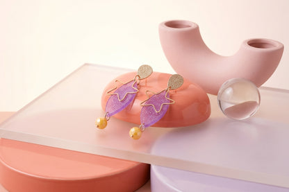 Purple Nina star geometric dangle earrings in a styled product setting