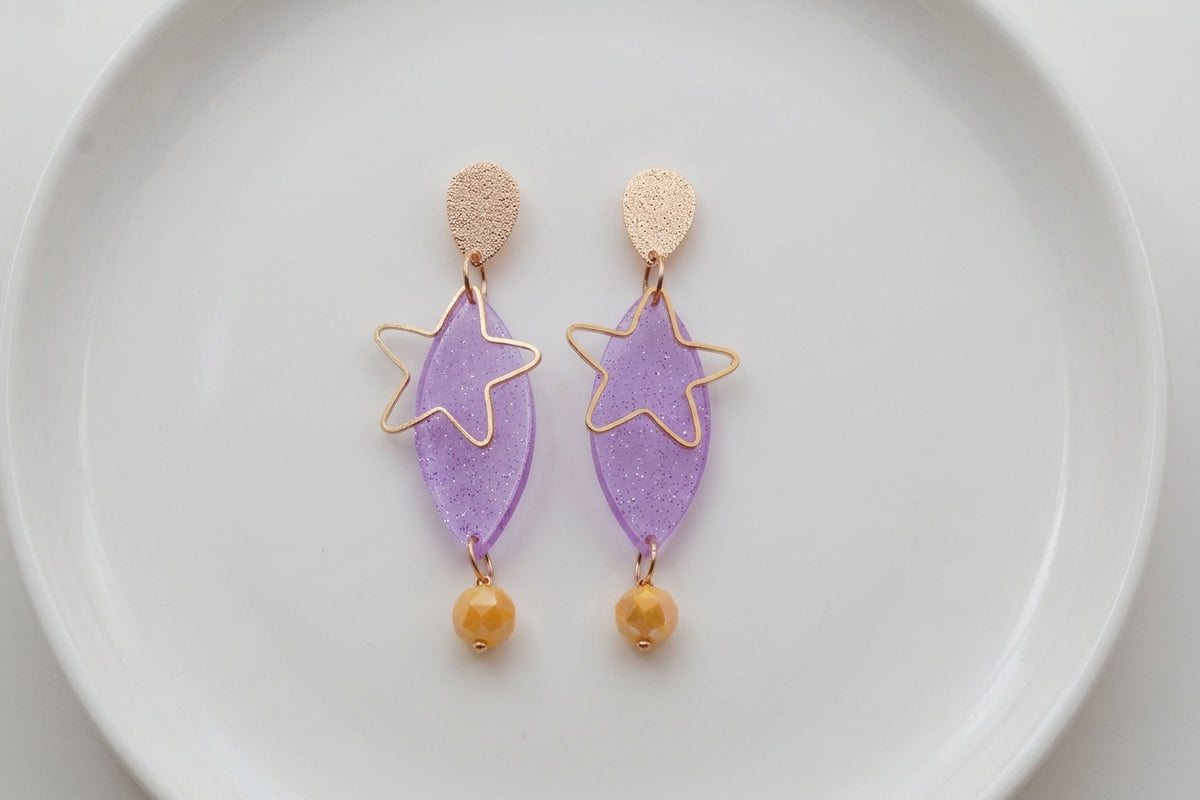Purple Nina star geometric dangle earrings arranged on a white plate