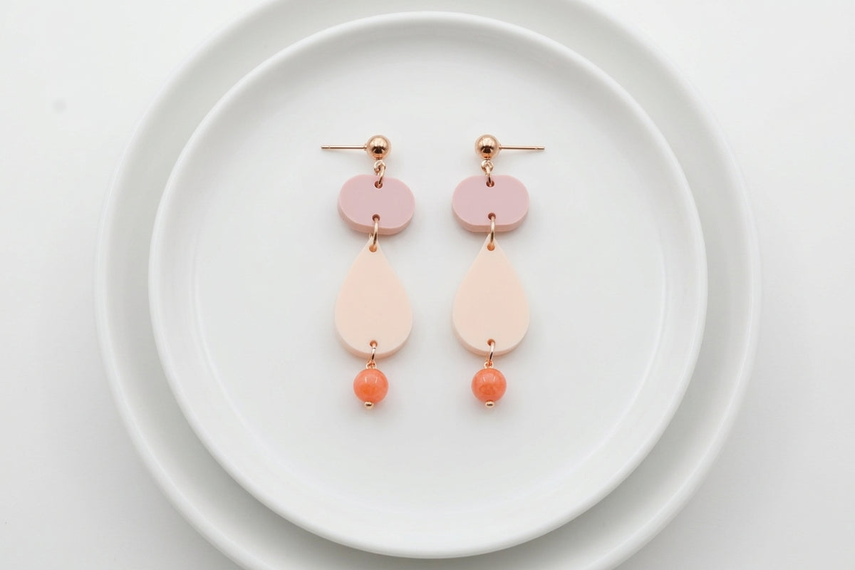 Beige Noor teardrop acrylic drop earrings arranged on a white plate
