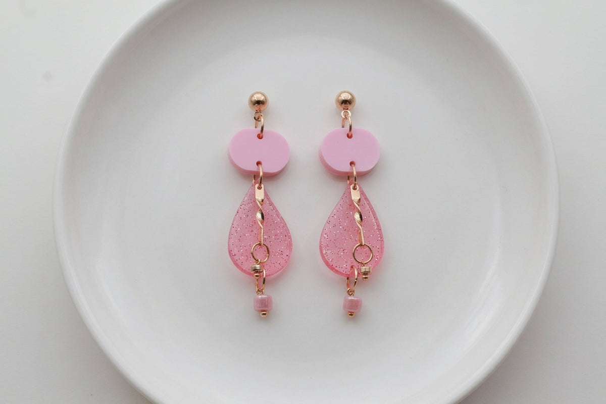 Pink Noor teardrop acrylic drop earrings arranged on a white plate