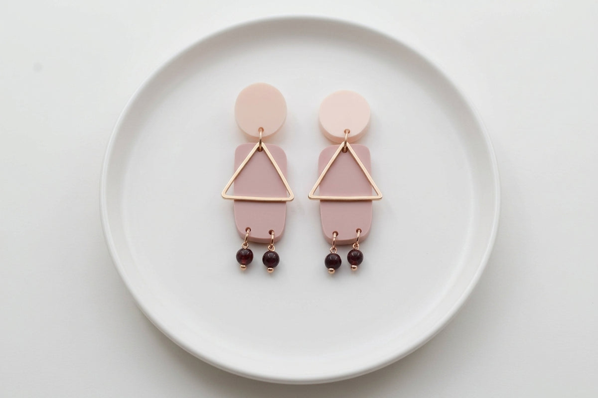 Beige Nora geometric rectangle dangle earrings arranged on a white plate