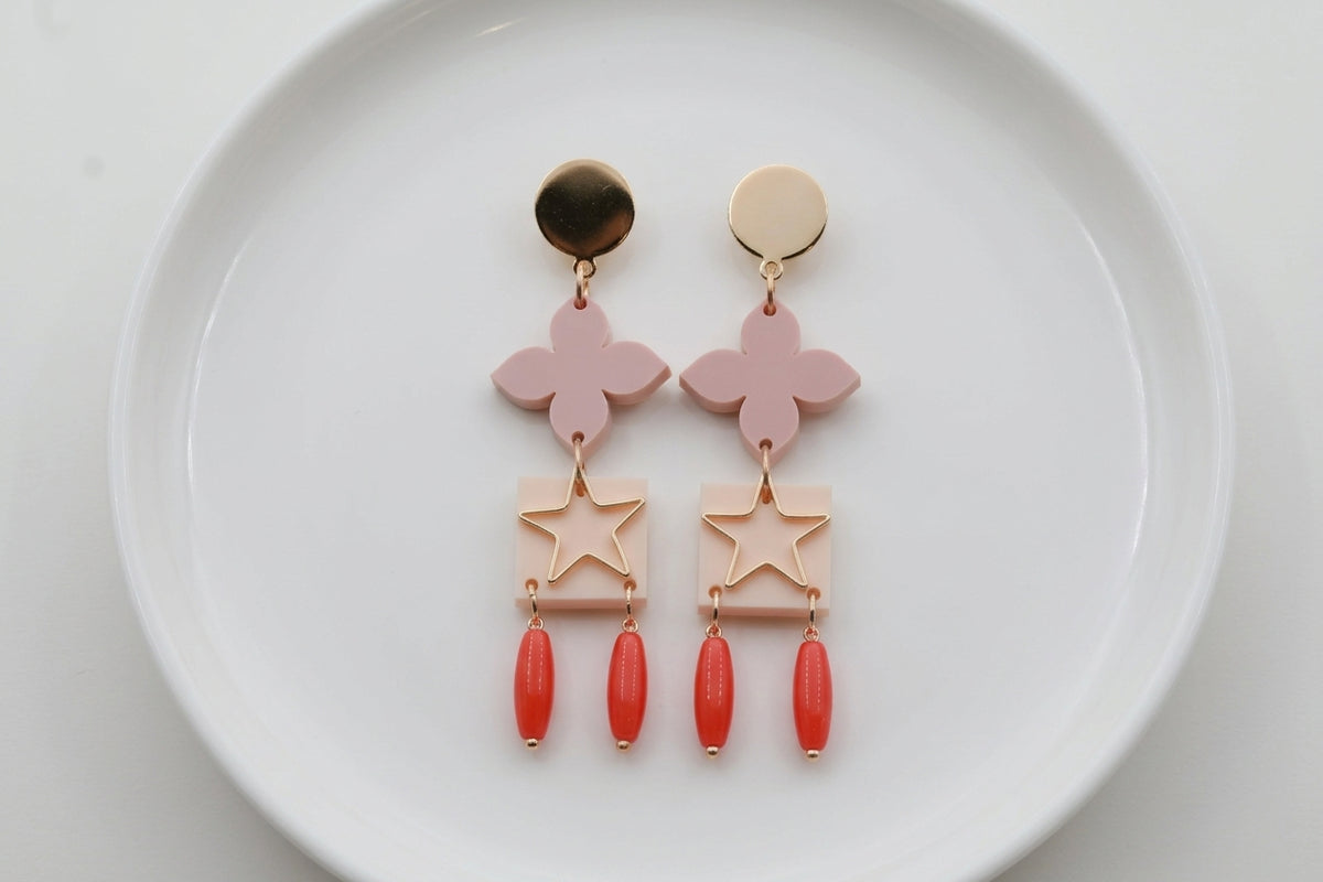 Beige Rose floral star drop earrings arranged on a white plate