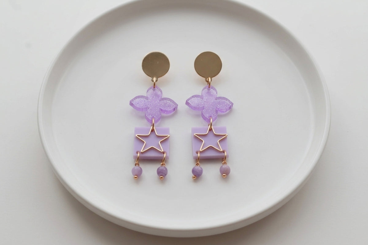 Purple Rose floral star drop earrings arranged on a white plate