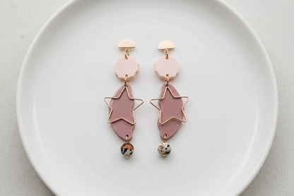 Beige Sara long star dangle earrings arranged on a white plate