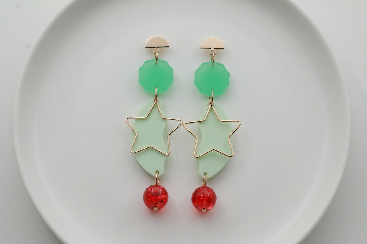 Green Sara long star dangle earrings arranged on a white plate