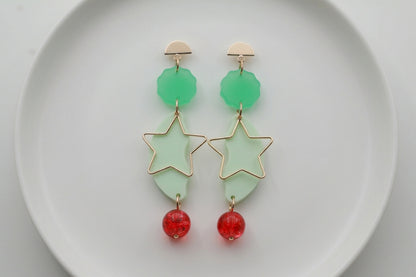 Green Sara long star dangle earrings arranged on a white plate