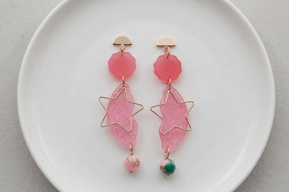 Pink Sara long star dangle earrings arranged on a white plate