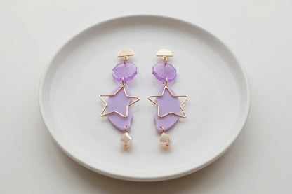 Purple Sara long star dangle earrings arranged on a white plate