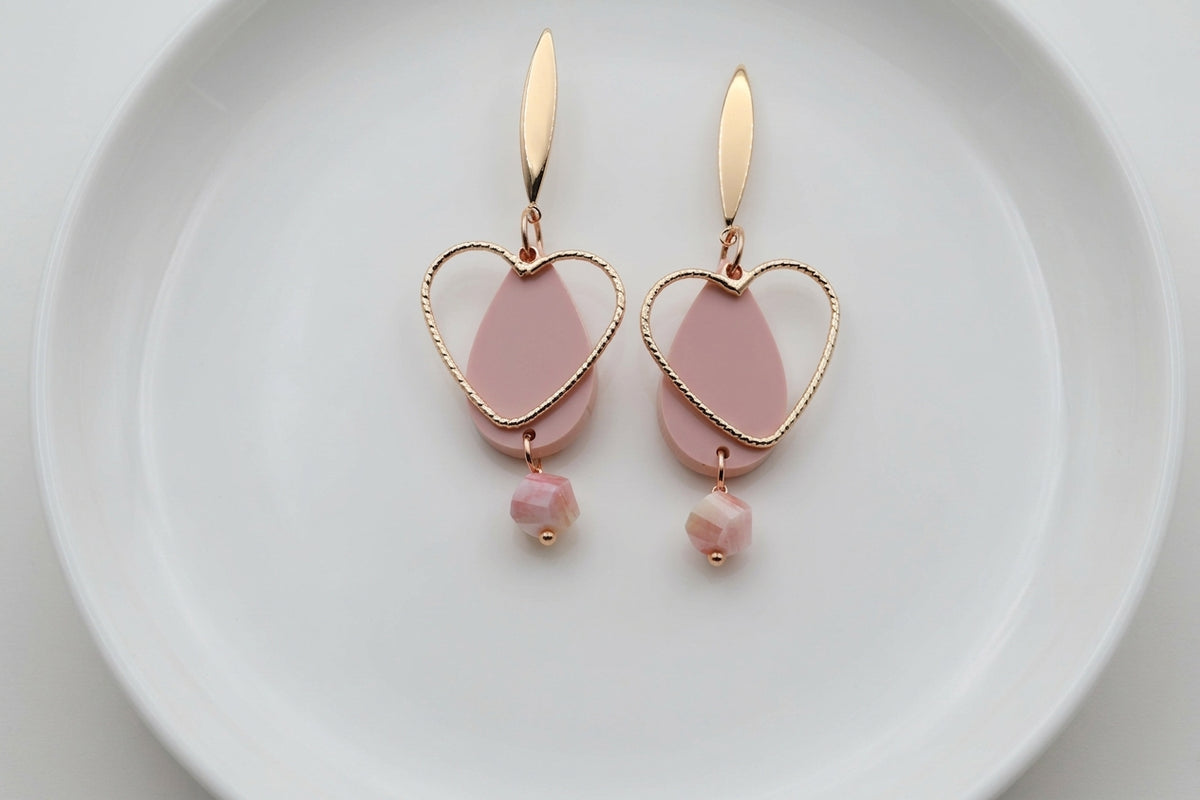 Beige Sofia heart teardrop dangle earrings arranged on a white plate