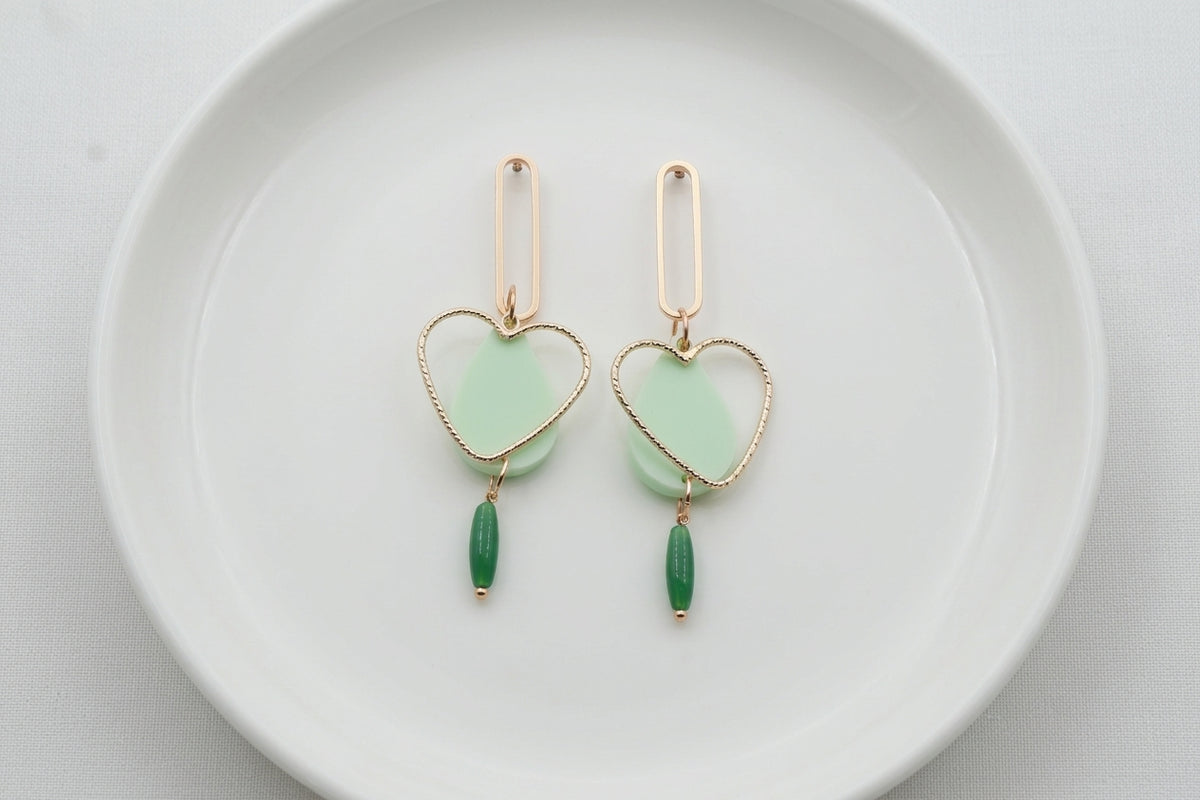 Green Sofia heart teardrop dangle earrings arranged on a white plate