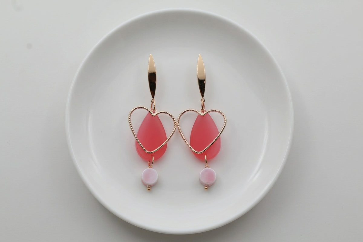 Pink Sofia heart teardrop dangle earrings arranged on a white plate
