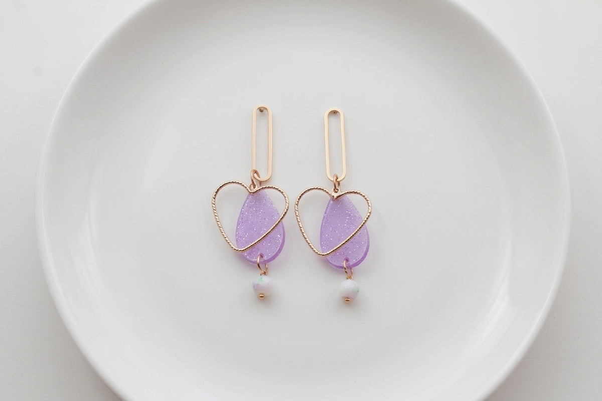 Purple Sofia heart teardrop dangle earrings arranged on a white plate