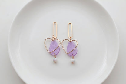 Purple Sofia heart teardrop dangle earrings arranged on a white plate