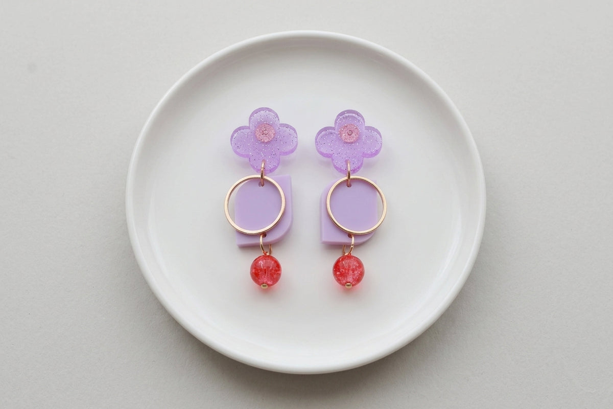 Purple Zoe floral geometric drop earrings arranged on a white plate