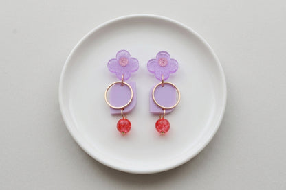 Purple Zoe floral geometric drop earrings arranged on a white plate